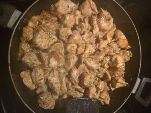 Cut up pieces of marinated chicken, cooking in a skillet.