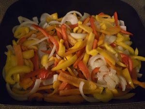 Onion strips and colorful bell pepper strips, cooking in an electric skillet.