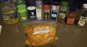 Cut up chicken in marinade in a gallon-size freezer bag, with various bottles of spices behind it.